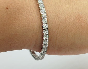 Puede incluir: Un brazalete de tenis de plata con una fila de diamantes brillantes.