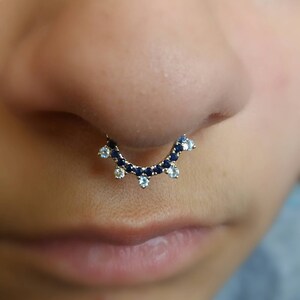 May include: A gold septum ring with blue and white gemstones