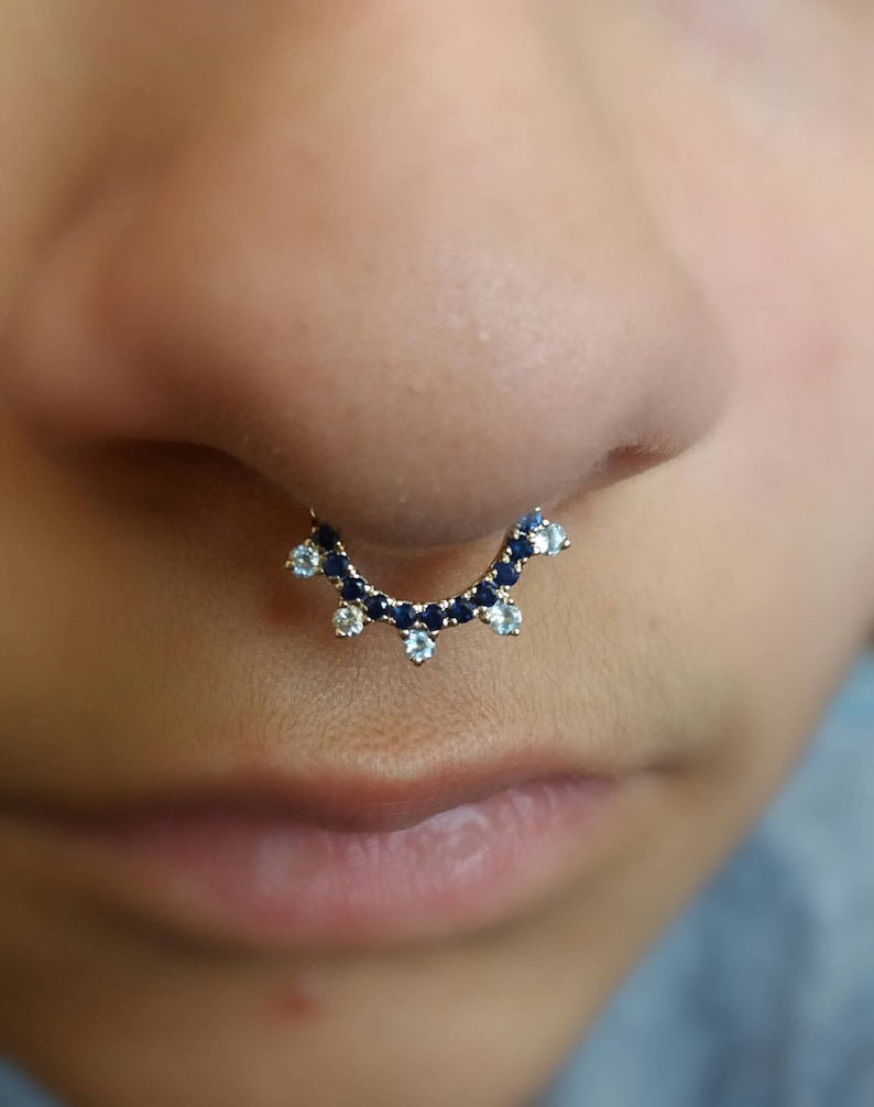 May include: A gold septum ring with blue and white gemstones