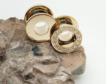 May include: Two gold ear gauges with a single row of clear cubic zirconia stones around the outer edge of the gauge.