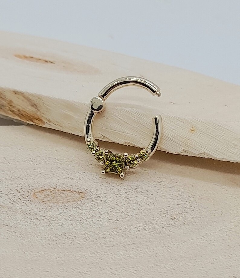 May include: A gold hoop earring with a row of small green gemstones and a larger square-shaped green gemstone in the center.