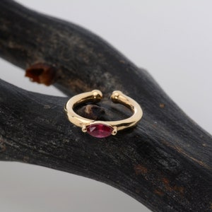 May include: Gold ear cuff with a single red gemstone. The cuff is open and has a rounded shape.