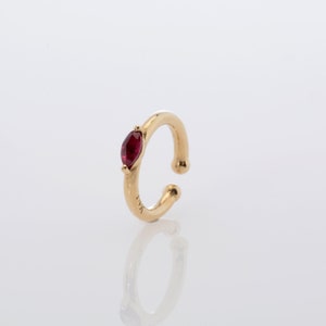 May include: Gold ear cuff with a single red gemstone.