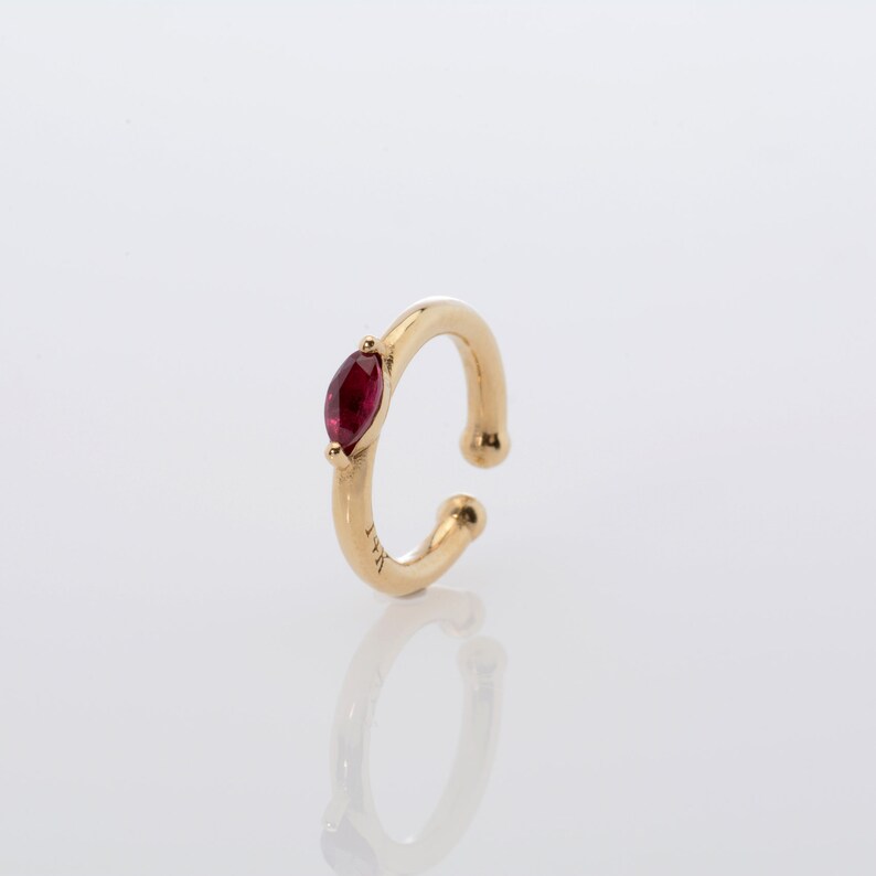 May include: Gold ear cuff with a single red gemstone.