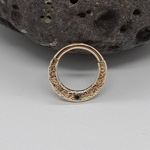 May include: Gold body jewelry with a textured finish and a small black gemstone.