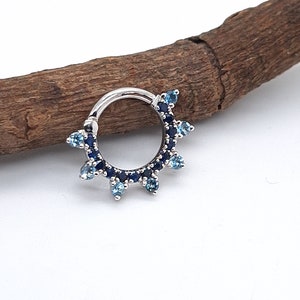 May include: A silver ring with a row of blue and light blue gemstones. The ring is set with a row of small gemstones around the band and larger gemstones at the top and bottom of the ring.
