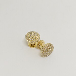 May include: Two gold-toned round earrings with a circular design of small, clear stones.