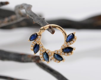 Puede incluir: Joyería corporal de oro con un diseño circular que presenta una fila de zafiros azules en forma de marquesa y diamantes transparentes más pequeños.