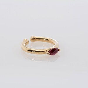 May include: Gold ear cuff with a single red gemstone.