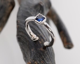 May include: A silver ring with a small, square, blue gemstone set in the center.