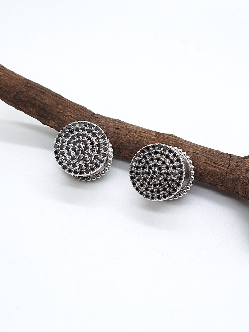 May include: A pair of silver stud earrings with a circular design. The earrings are set with black stones in a concentric circle pattern.