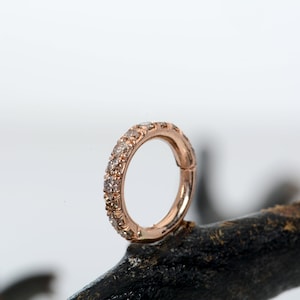 May include: A rose gold clicker earring with a row of small diamonds around the band.