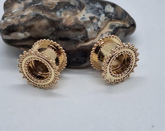 May include: Two gold-colored ear gauges with a sunburst design. Each gauge features a series of small, raised beads around the outer edge and inner circle. The gauges are displayed on a light background.