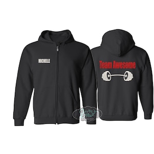 May include: Black zip-up hoodie with the name "Michelle" in white on the front. The back of the hoodie features the text "Team Awesome" in red with a barbell graphic. The hoodie has a hood and a full-length zipper.