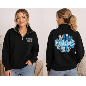 May include: A black quarter-zip sweatshirt featuring the text COACH JENN on the left chest. The back displays a large circular graphic of a blue and silver pom-pom with the word BULLDOGS written across the center in a bold blue font.