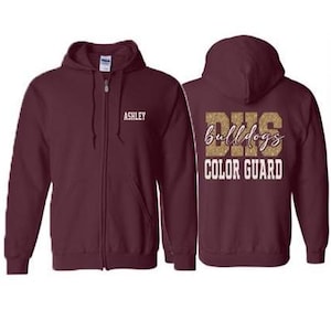 May include: Burgundy zip-up hoodie with the name "Ashley" embroidered on the front. The back of the hoodie features the text "DHS Bulldogs COLOR GUARD" in a glittery gold and white design. The hoodie has a hood and a full-length zipper.