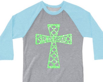 May include: A grey and light blue baseball tee shirt with a green cross and the text "He is risen".