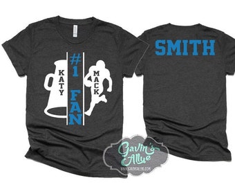 May include: A dark grey t-shirt with a white silhouette of a football player and a megaphone with the text "#1 KATY FAN" in blue and white. The back of the shirt has the text "SMITH" in blue.