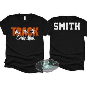 May include: Two black t-shirts. One shirt has the text "TRACK GRANDMA" in orange with white silhouettes of runners. The other shirt has the text "SMITH" in white.