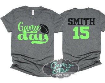 Könnte beinhalten: Zwei graue T-Shirts, eines mit dem Text "Game day" in Grün mit einer Fußballabbildung und das andere mit dem Text "SMITH 15" in Schwarz und Grün.