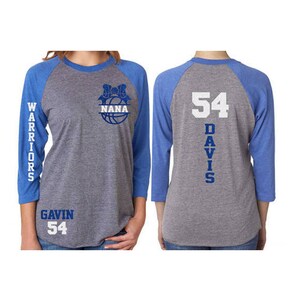 Pu&ograve; includere: Una maglietta da baseball grigia e blu con una grafica di pallacanestro sul davanti e il testo "NANA" all'interno della palla. La manica sinistra ha il testo "WARRIORS" e la manica destra ha il testo "DAVIS 54". La parte posteriore della maglietta ha il testo "DAVIS 54" verticalmente sulla schiena.