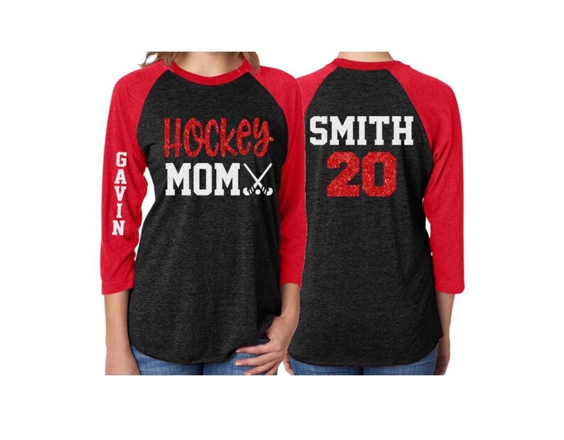 May include: Black and red baseball style shirt with the text "Hockey Mom" and hockey sticks on the front and the text "SMITH 20" on the back.