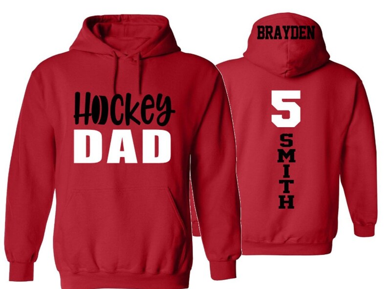 Op de afbeelding: Rood hoodie met de tekst "Hockey Dad" in zwart en wit op de voorkant en de tekst "Brayden Smith 5" in zwart op de achterkant.
