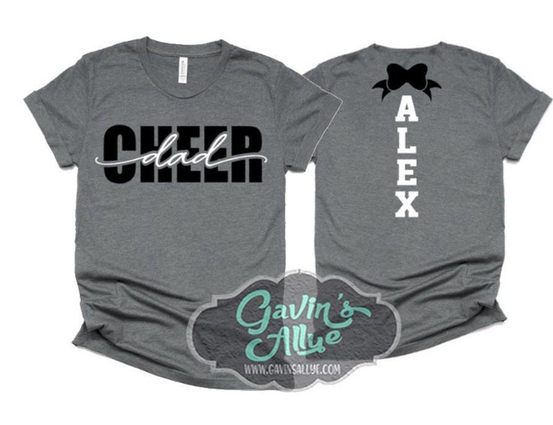 Pode incluir: Duas camisas cinzas com texto preto. Uma camisa diz "Cheer dad" e a outra diz "ALEX" com um la&ccedil;o preto no topo.