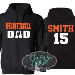 May include: Black hooded sweatshirt with the text "Football Dad" in white with orange football players and a football on the front. The left sleeve has the name "Alex" in white. The back of the sweatshirt has the text "Smith 15" in white with orange outlines.