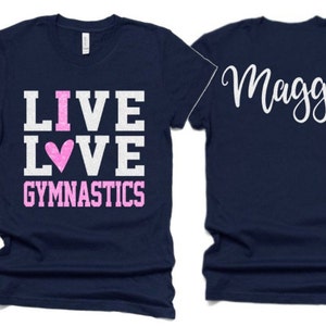K&ouml;nnte beinhalten: Zwei marineblaue T-Shirts. Ein Shirt hat den Text "I LIVE LOVE GYMNASTICS" in Wei&szlig; mit einem rosa Herzen. Das andere Shirt hat den Namen "Maggie" in wei&szlig;er Kursivschrift.