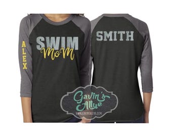 May include: A black and gray raglan style shirt with the words "SWIM Mom" in gray and yellow. The name "ALEX" is printed vertically on the left sleeve. The back of the shirt says "SMITH" in gray.