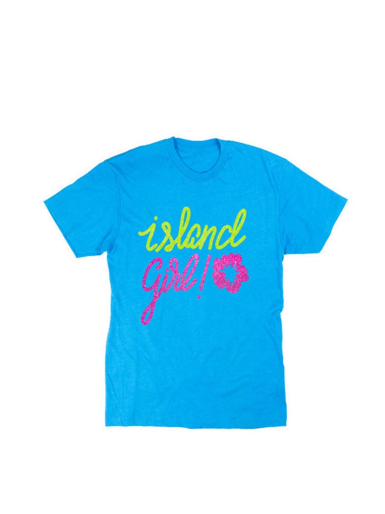 May include: A turquoise blue t-shirt with the text "island girl!" in green and pink glitter.