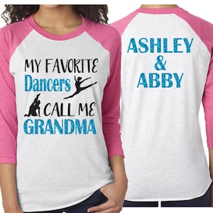 May include: A white and pink baseball tee shirt with the text "My Favorite Dancers Call Me Grandma" on the front and "Ashley & Abby" on the back. The shirt features a silhouette of a dancer in a blue glitter design.