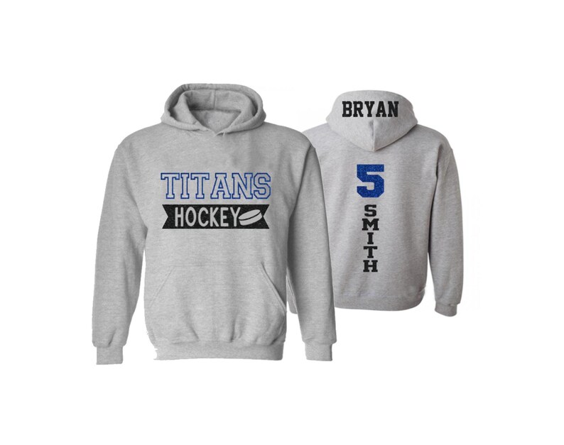 May include: Gray hooded sweatshirt with the text "Titans Hockey" and a hockey puck graphic on the front. The back of the sweatshirt has the text "BRYAN SMITH" and the number "5" in blue.