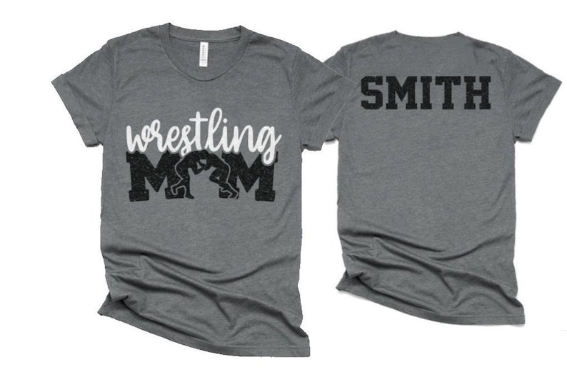 May include: A gray t-shirt with the text "wrestling mom" in white with a black silhouette of two wrestlers. The back of the shirt has the text "SMITH" in black.