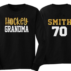 May include: Two black long-sleeved shirts with gold glitter lettering. One shirt says "Hockey Grandma" and the other says "Smith 70".