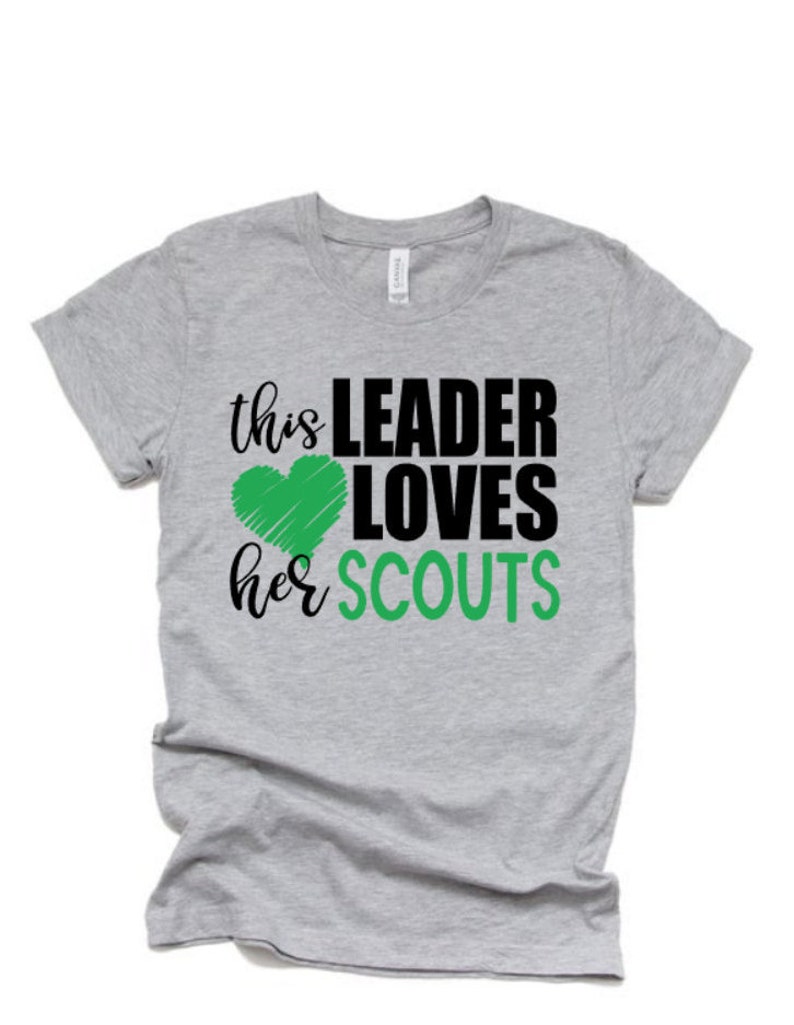 May include: Gray t-shirt with the text "this LEADER LOVES her SCOUTS" in black and green. A green heart is drawn next to the word "LOVES".
