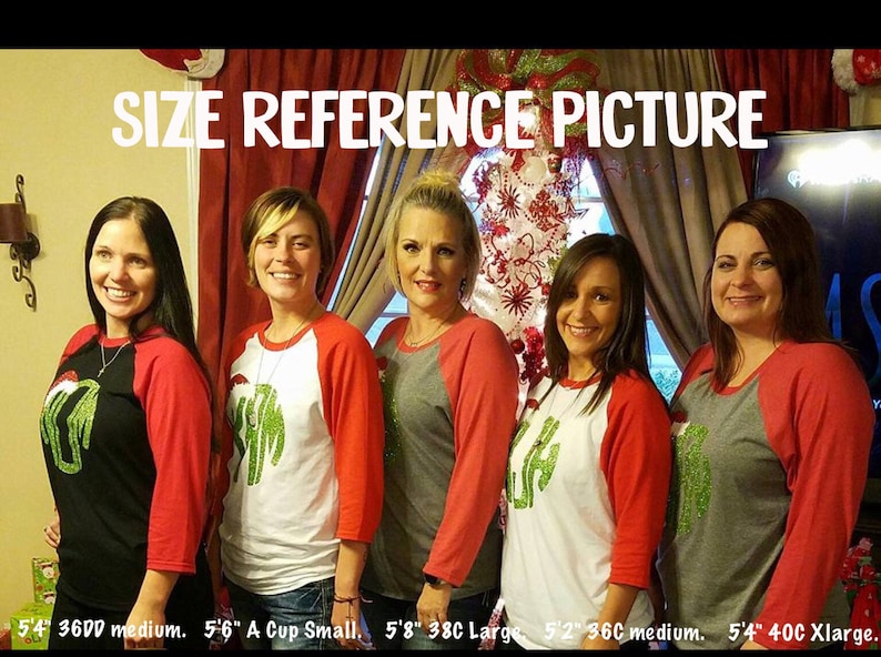 May include: Four women wearing red and grey baseball shirts with green glitter designs. The shirts have the text "SIZE REFERENCE PICTURE" at the top. The women are standing in front of a Christmas tree and a wall with a red curtain. The text at the bottom of the image reads "5'4" 3600 medium. 5'6" A Cup Small, 5'8" 38C Large, 5'2" 36C medium. 5'4" 40C Xlarge."