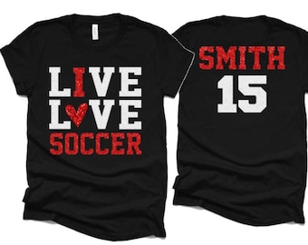 May include: Two black t-shirts with red glitter text. One shirt says "LIVE LOVE SOCCER" with a red heart. The other shirt says "SMITH 15".