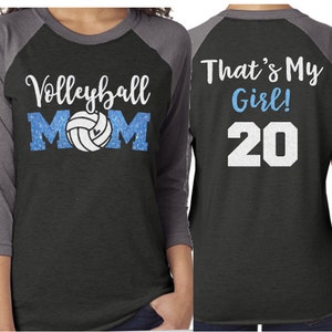 May include: A black and gray raglan-style shirt with the words "Volleyball MOM" in white and blue, and a volleyball graphic. The sleeve has the name "ALEX" in white. The back says "That's My Girl!" and the number "20".
