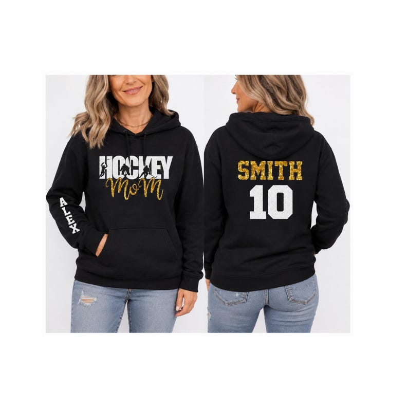Peut inclure: Un sweat-shirt &agrave; capuche noir avec le texte blanc HOCKEY MOM et des silhouettes de joueurs de hockey sur le devant, le nom ALEX en blanc sur la manche, et le nom SMITH en paillettes dor&eacute;es avec le num&eacute;ro 10 en blanc au dos.