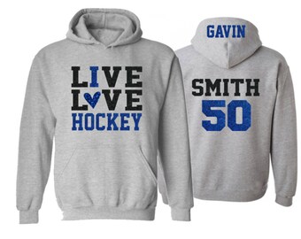 May include: Gray hooded sweatshirt with the text "I LIVE LOVE HOCKEY" on the front and the text "GAVIN SMITH 50" on the back. The text is in black with blue glitter accents.