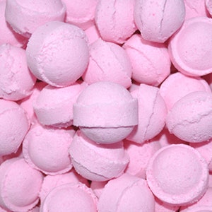 May include: A close-up image of a large pile of pink bath bombs. The bath bombs are round and have a smooth, slightly textured surface.