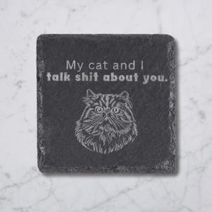 May include: Square black slate coaster with the text "My cat and I talk shit about you." A detailed illustration of a cat is below the text. The coaster has a rough, textured surface.
