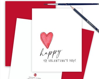 May include: A white card with a red watercolor heart and the text "happy 1st VALENTINE'S DAY!" printed in black. The card is on a red background.