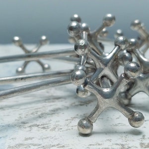 May include: A set of silver cocktail stirrers shaped like a game of jacks. The stirrers are arranged in a pile, with the tips of the stars pointing in different directions.