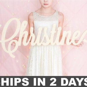 May include: A large, wooden sign with the name "Christine" written in a cursive font. The sign is held by a person wearing a white dress.