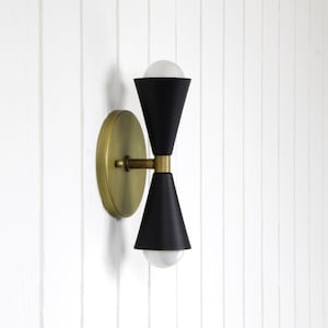 May include: A black and gold wall sconce with two light bulbs. The sconce has a cone-shaped design and a round base.