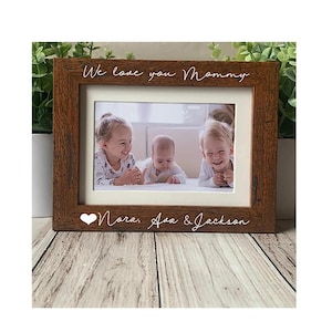 May include: A brown wooden picture frame with a white mat, displaying a photo of three children. The frame has the text "We love you Mommy" and "Nora, Ava & Jackson" in white script.