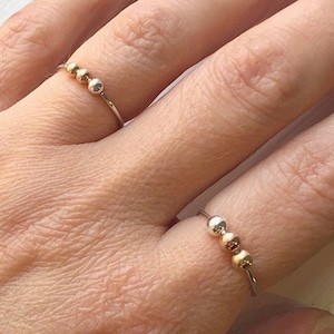 May include: Two silver rings with gold beads. The rings are worn on the index and middle fingers of a hand.